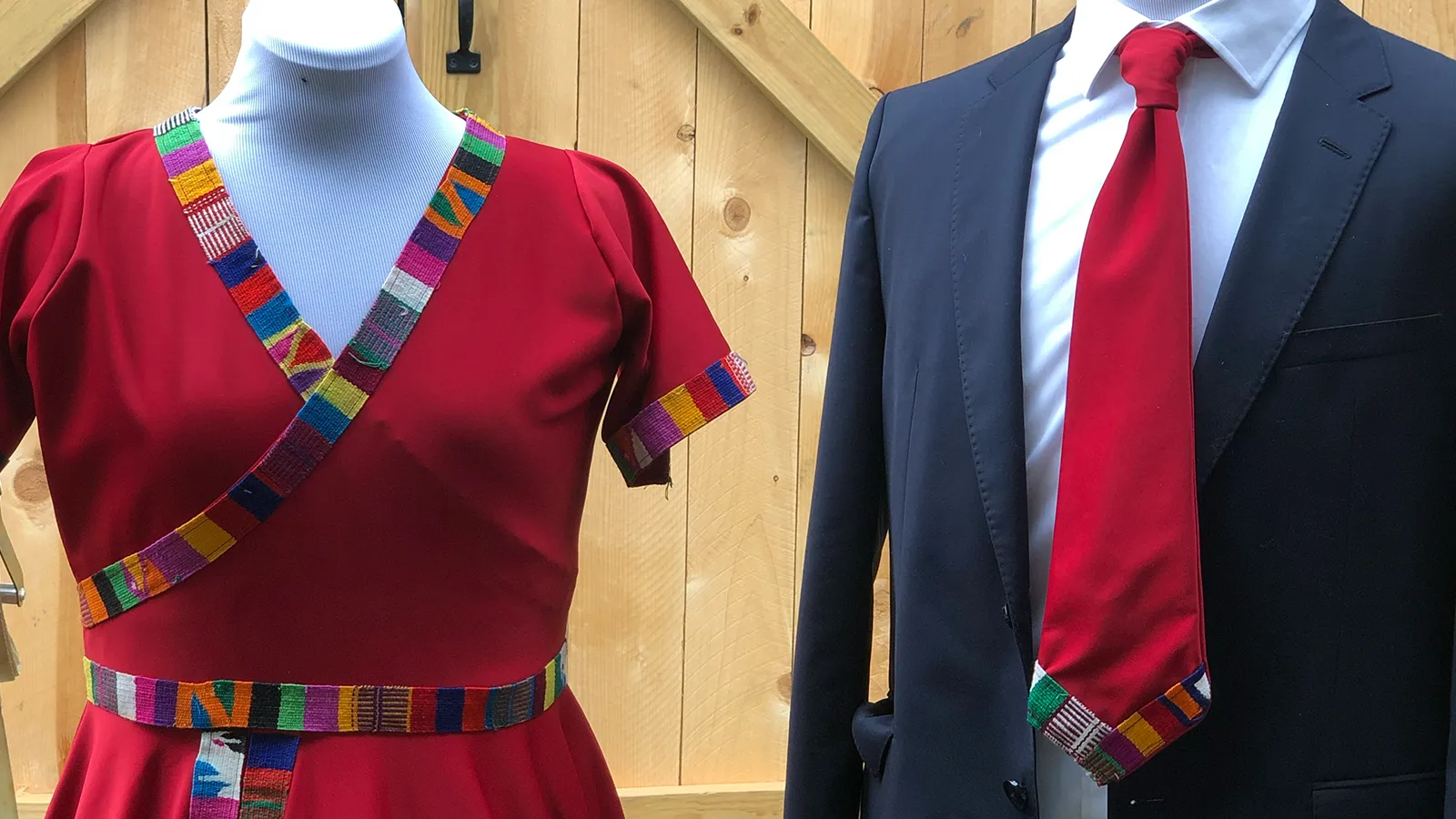 The wedding outfits on dress forms: a red dress and a navy suit, both trimmed with woven Guatemalan ribbon
