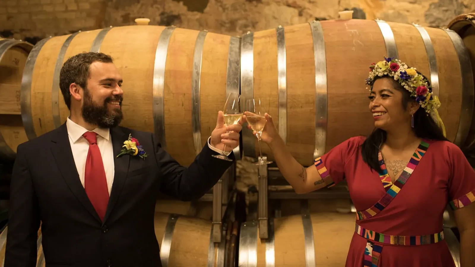 Peter and Consuelo raising a toast in front of a row of wine barrels