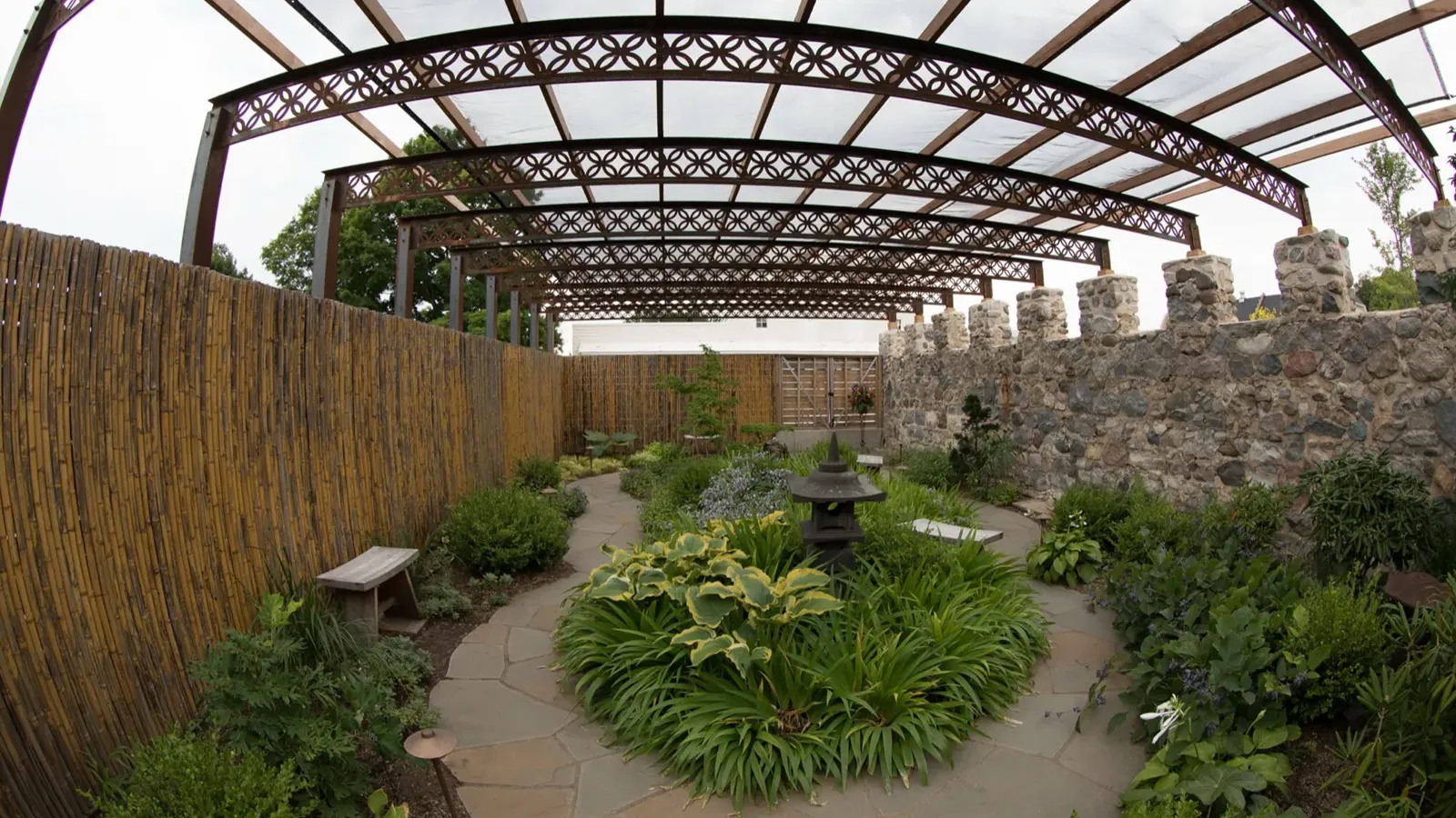 A walled garden of stone and pergola beams, planted along a flagstone path